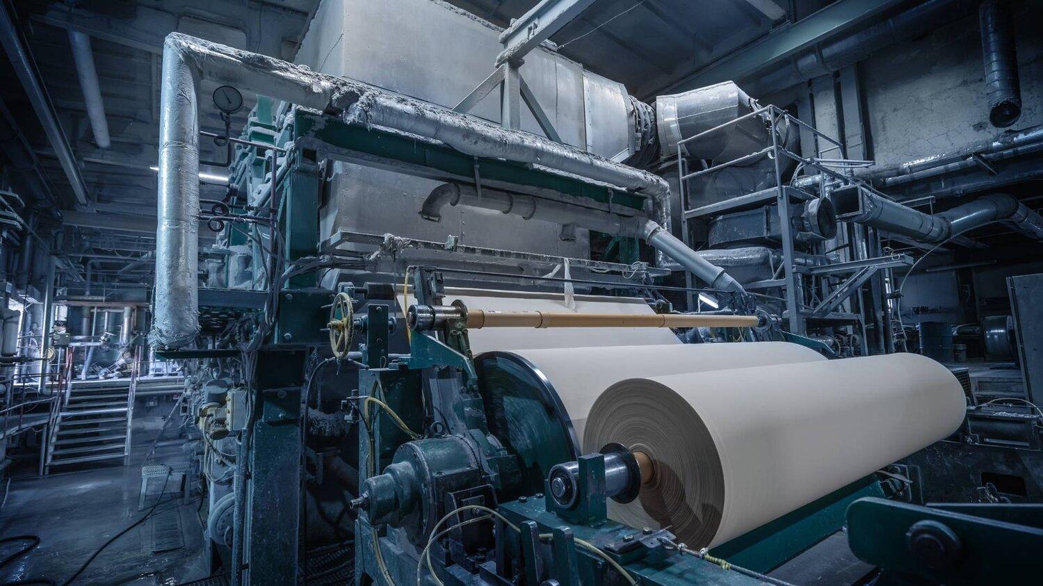 Wide paper reel and industrial rollers inside a paper mill